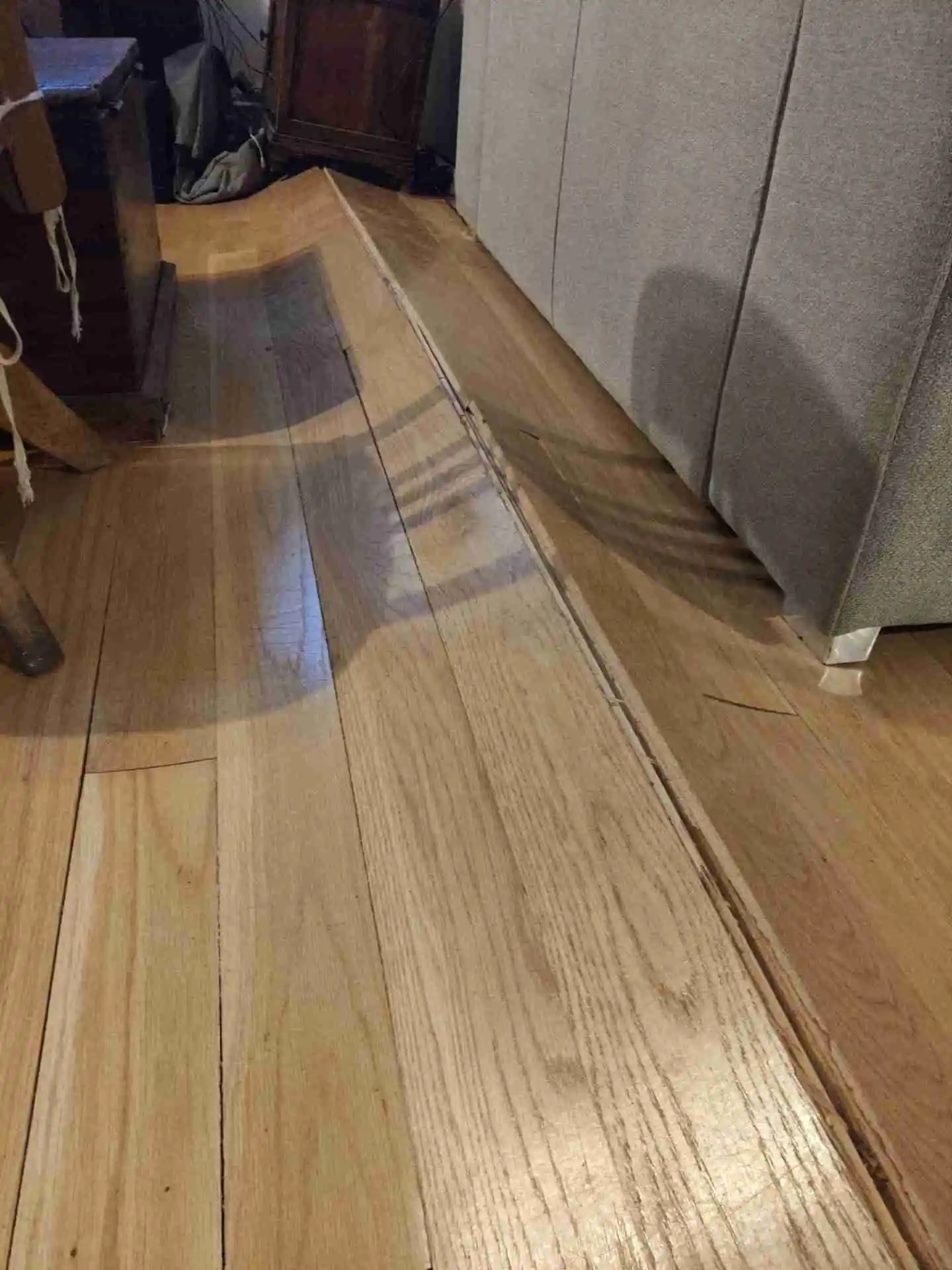 Tarima de madera hinchada y levantada por humedad bajo un mueble