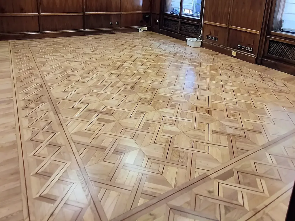 Suelo de tarima de castaño con cenefas de roble y nogal en una sala con paredes de madera