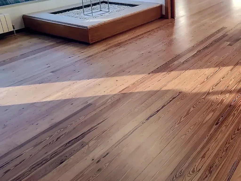 Suelo de pino melis de veta marcada con una franja de sol y otra de sombra, junto a una plataforma de madera con grava blanca