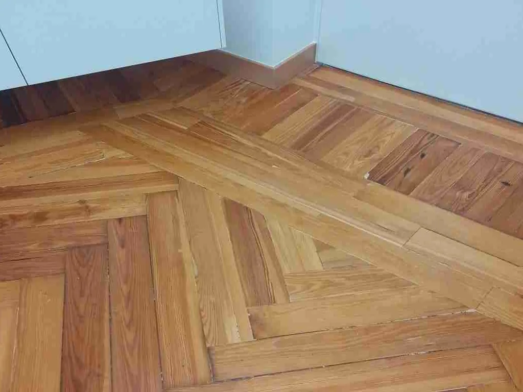 Suelo de pino melis en espiga con faja, de tono ámbar y anaranjado, junto a un mueble blanco