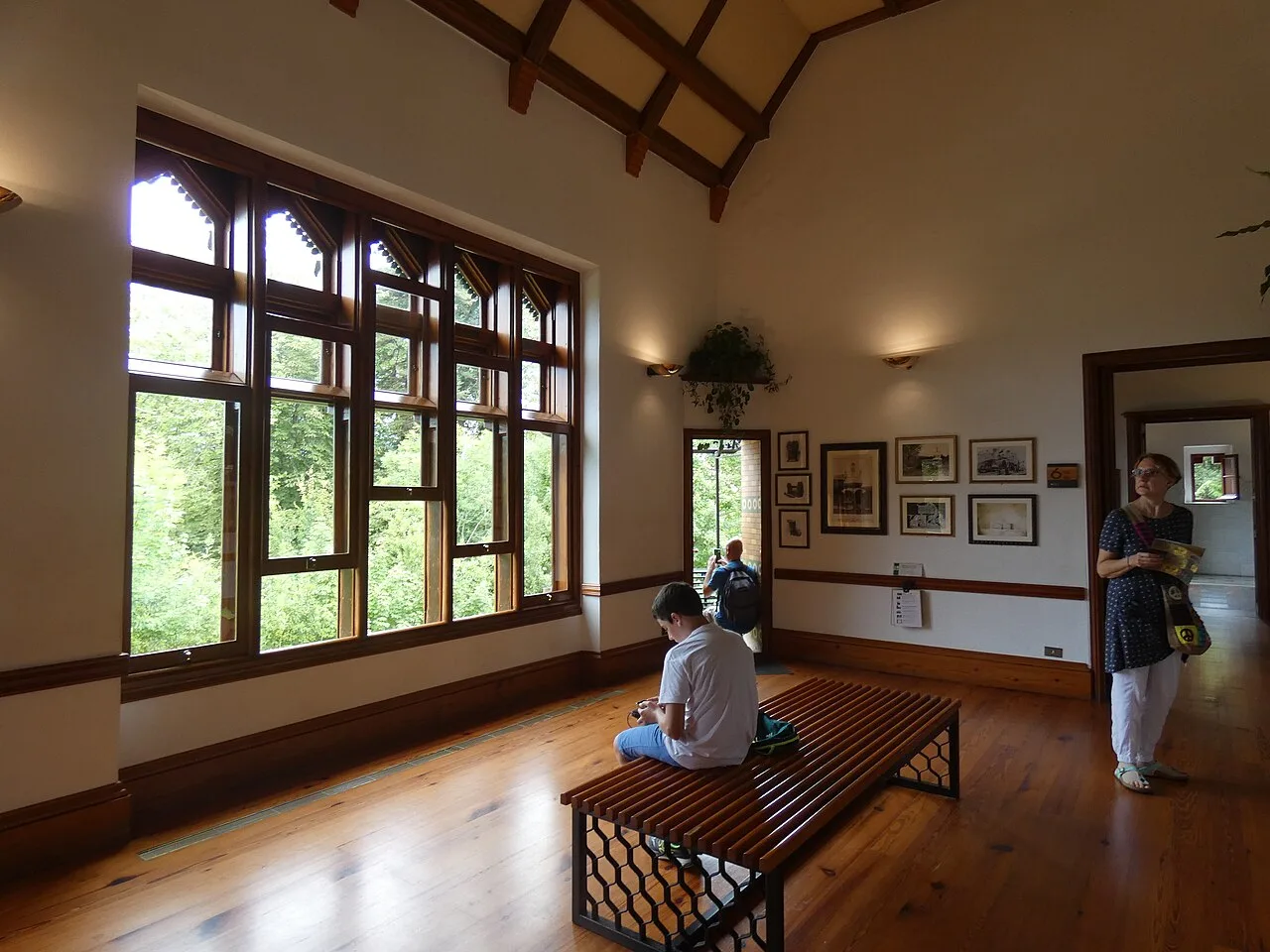 Salón principal de El Capricho con un ventanal de madera, un banco y suelo de tablas de tono miel con una rejilla metálica estrecha junto al zócalo
