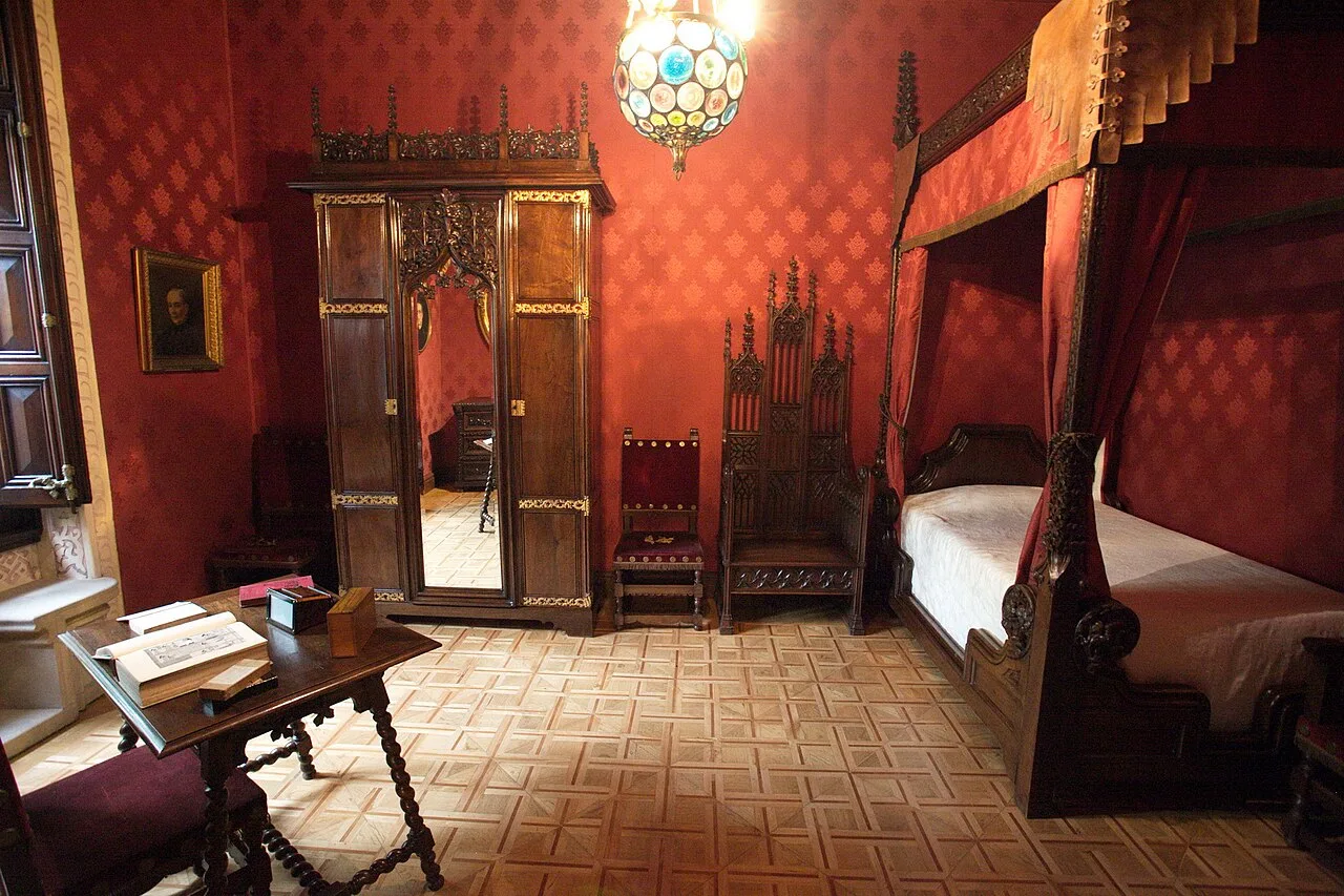 Dormitorio de paredes rojas con cama de dosel y armario de luna sobre un parqué claro de losas cuadradas con aspa