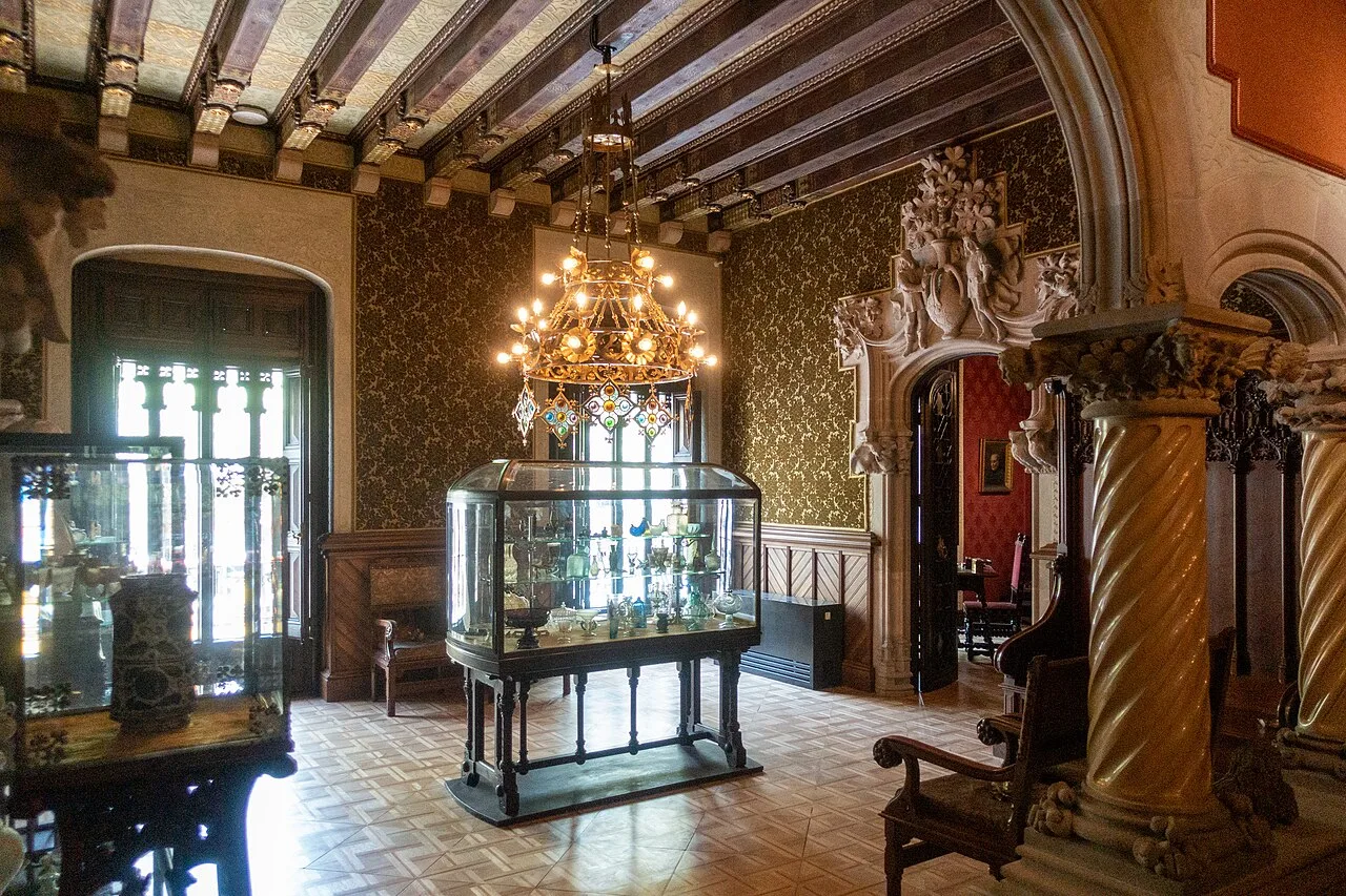 Sala de papel verde con una lámpara de bronce y una vitrina en el centro sobre un parqué de losas cuadradas claras, con columnas salomónicas a la derecha