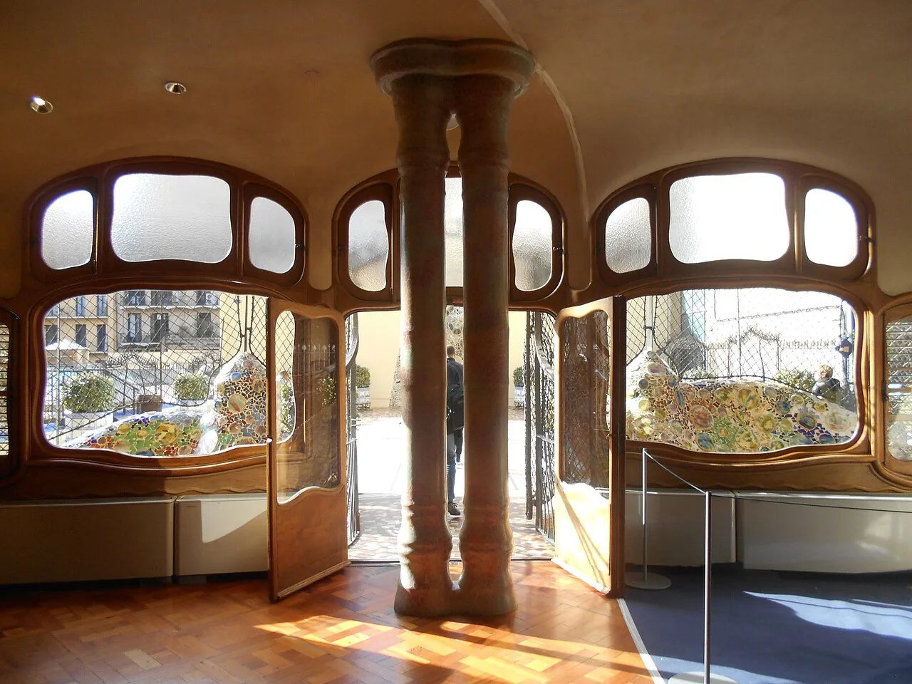 Comedor de la Casa Batlló con columnas dobles ante las puertas abiertas al patio, suelo de losetas de tablillas al sol y una moqueta azul a la derecha