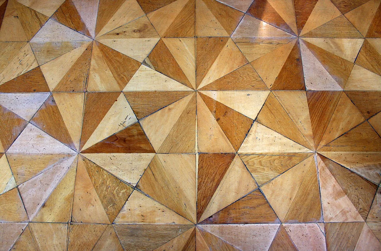 Detalle de un parqué de triángulos de madera clara y color miel que forman estrellas de doce puntas
