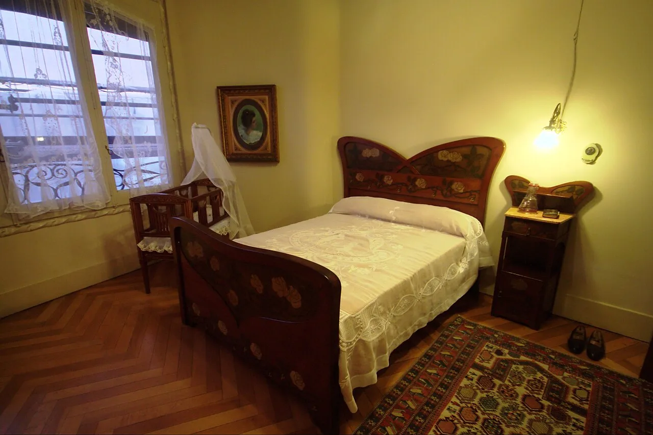 Dormitorio con cama de madera pintada con flores, cuna y alfombra sobre un parqué de espiga rojizo