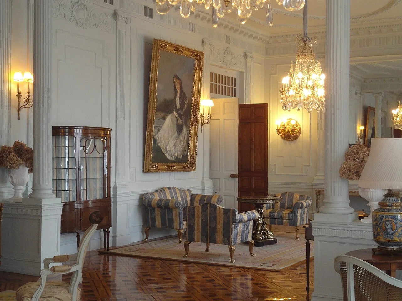 Salón con columnas, sofás de rayas y retrato de la reina sobre un parquet oscuro de paños en diagonal