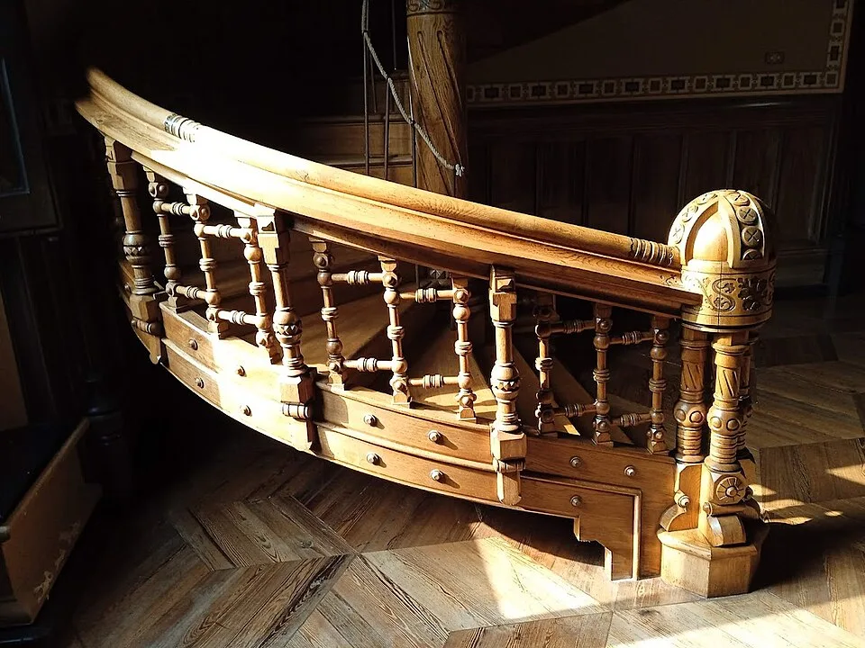 Escalera de caracol de madera tallada que arranca sobre un suelo de madera en espiga