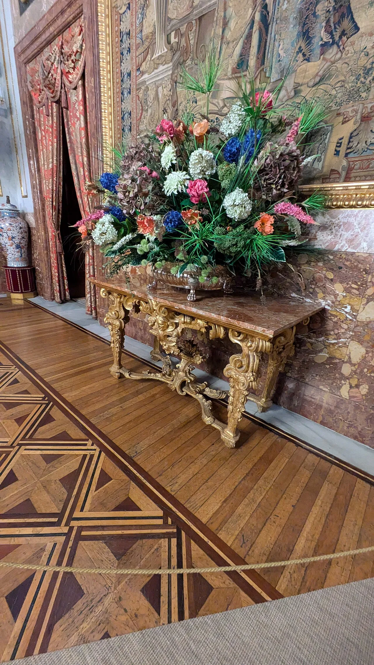 Detalle del parquet del Comedor de Gala, con paños de rombos y una faja de borde junto a una consola dorada