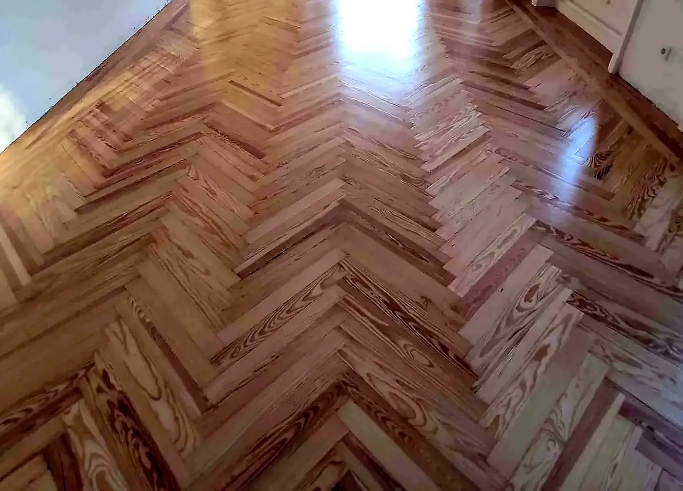 Suelo de pino melis viejo en espiga, con barniz reciente, junto a una pared blanca y un mueble