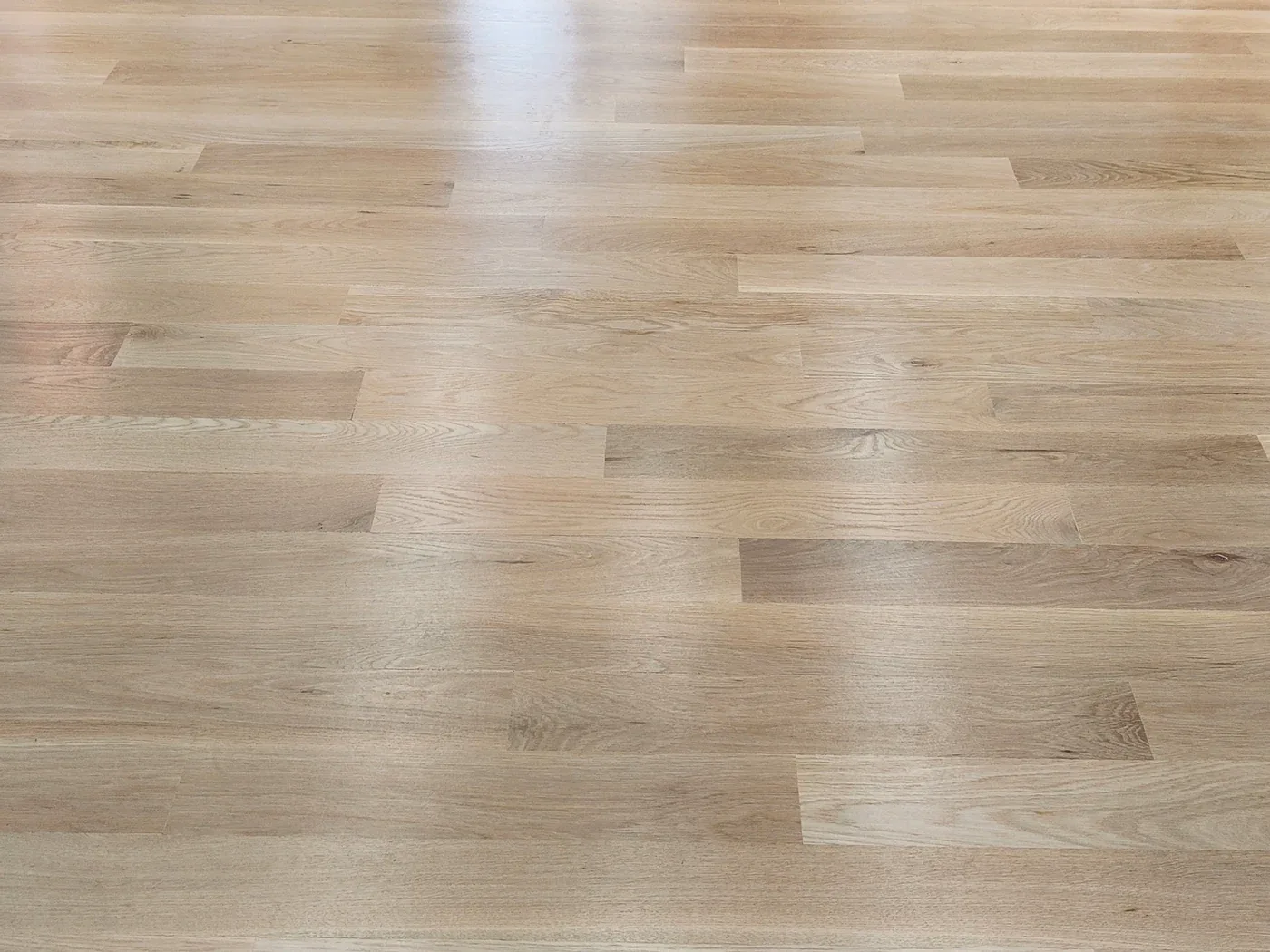 Suelo de tablas anchas de madera clara, con un reflejo de luz en la superficie